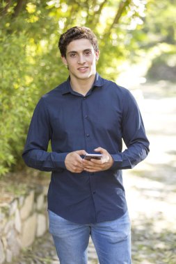 Kamera ve manifatura doğru telefon üzerinde yürüme gülümseyen genç bir işadamı portresi önden görünüm