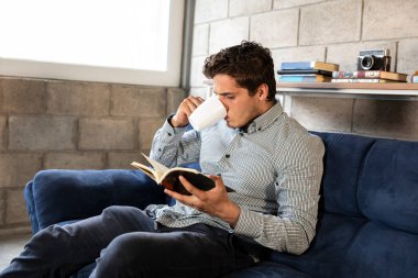 Yakışıklı ve zarif bir adam oturma odasında COVID-19 salgını sırasında kitap okuyor.