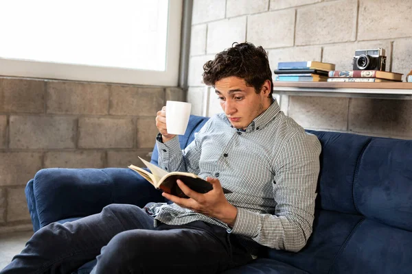 Yakışıklı ve zarif bir adam oturma odasında COVID-19 salgını sırasında kitap okuyor.