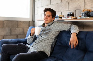 Yakışıklı ve zarif bir adam kahve içiyor. Oturma odasındaki COVID-19 salgını sırasında...