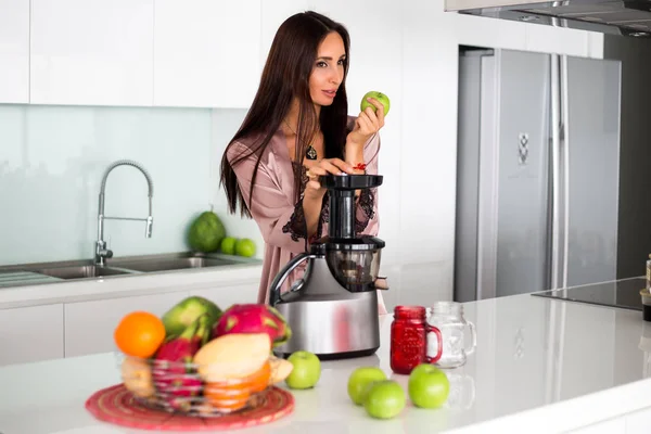 young beautiful girl in the kitchen in the morning preparing fresh smoothies juice in a blender of their apple and tropical fruits and vegetables, healthy food, detox
