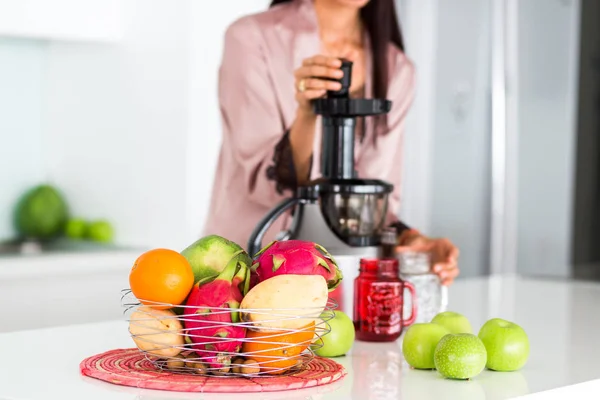 young beautiful girl in the kitchen in the morning preparing fresh smoothies juice in a blender of their apple and tropical fruits and vegetables, healthy food, detox