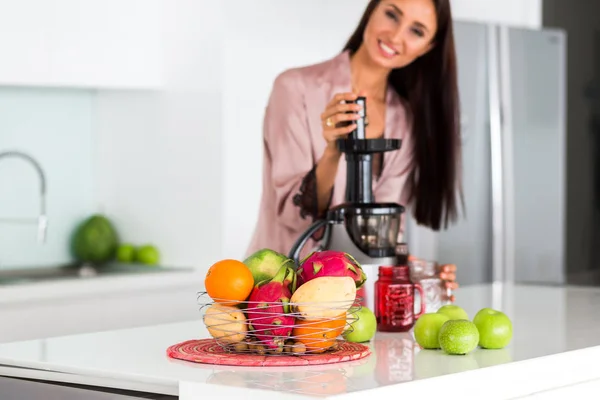 young beautiful girl in the kitchen in the morning preparing fresh smoothies juice in a blender of their apple and tropical fruits and vegetables, healthy food, detox