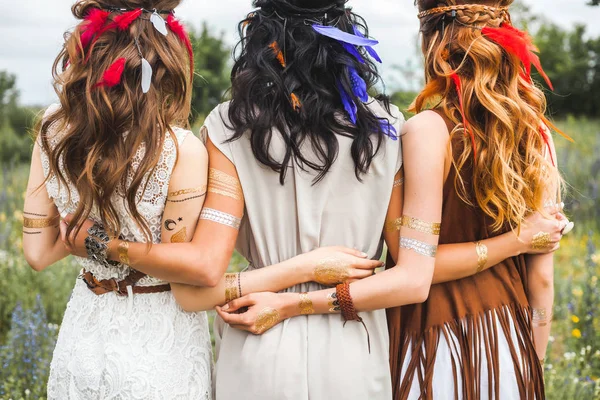 Rear view of hippie girls with feathers in long hair posing on nature background