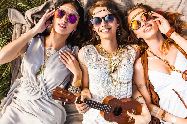 Three young hippie girls lying with guitar on plaid outdoors