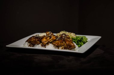 Teriyaki tavuk beyaz plaka ve koyu arka plan.