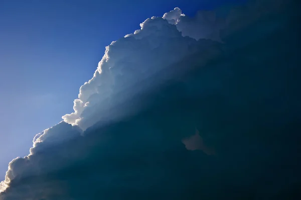 The cloud on one side is lighted with sunlight on the background of a blue sky.