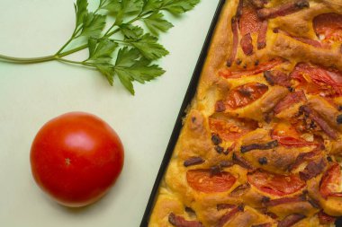  Parlak, iştah açıcı et ve domatesli pizza fotoğrafı. Pizzanın yanında bir domates ve maydanoz yaprağı var..