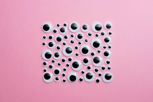 Many googly eyes organized over pink background