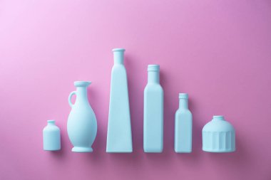 Pembe arka plan üzerinde bir satırda düzenlenen renkli boyalı cam şişeler