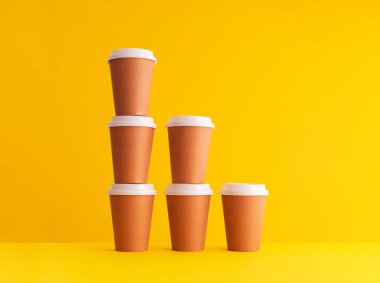 Multiple disposable coffee cups organized in a stack over yellow background clipart