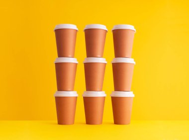 Birden çok tek kullanımlık kahve fincanı bir yığın içinde sarı arka plan üzerinde düzenlenir.