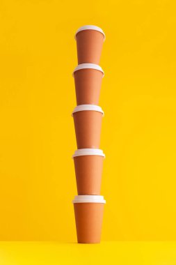 Birden çok tek kullanımlık kahve fincanı bir yığın içinde sarı arka plan üzerinde düzenlenir.