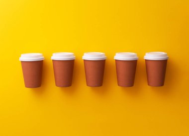Birden çok tek kullanımlık kahve bardağı sarı arka plan üzerinde organize