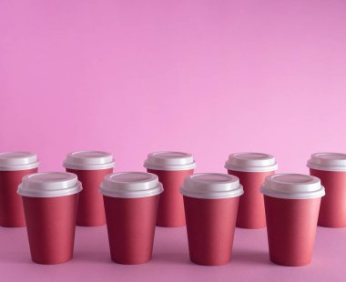 Pembe arka plan üzerinde düzenlenen tek kullanımlık kahve bardağı