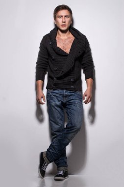 Örgü süveter giyen yakışıklı bir adam arka planda poz veriyor.