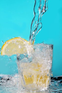 Su bardağa doluyor mavi arka planda limon ile