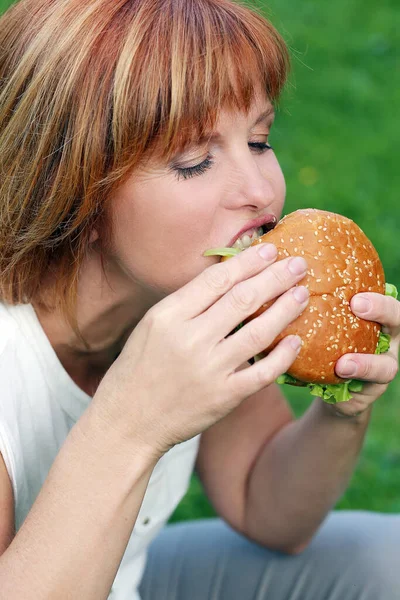 公園でハンバーガーを食べている魅力的な女性の肖像画 — ストック写真