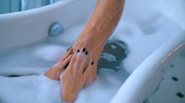 Lüks banyoda köpükle rahatlayan seksi genç kadın.