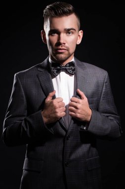 Siyah arka planda poz veren takım elbiseli yakışıklı bir adamın portresi.