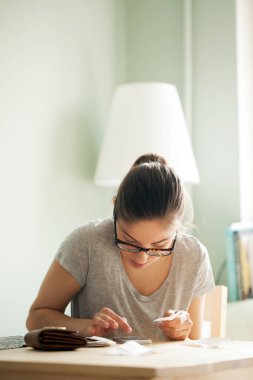 Gözlüklü kadın telefonundaki çeklerden bir şeyler sayıyor.