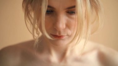 Sarı saçlı, bej arka planda kameraya poz veren doğal bir genç kadın portresi. 