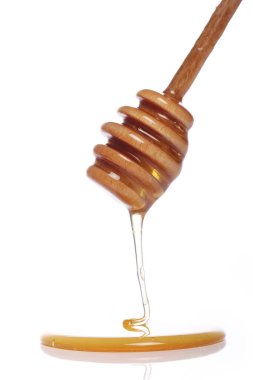 Beyaz arka planda tahta kaşıktan bal damlıyor.
