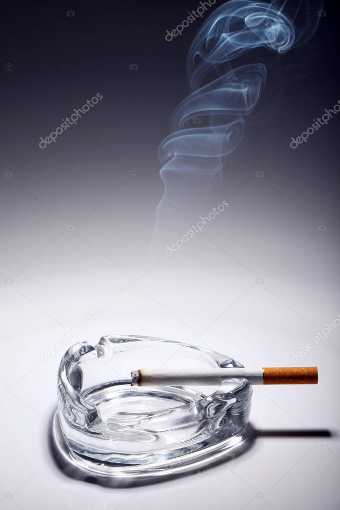 Cigarette in the ashtray over gray gradient
