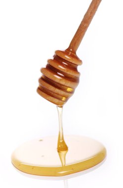 Beyaz arka planda tahta kaşıktan bal damlıyor.