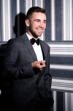 şeritli bir arka plan üzerinde koyu takım elbise ve kravat takan yakışıklı adam sakallı bir poz