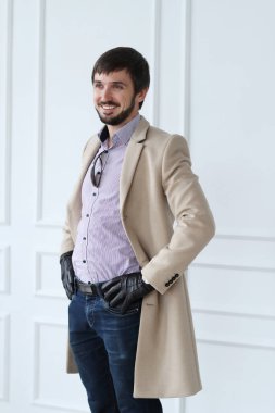 Beyaz duvar arkasında poz veren ceketli yakışıklı bir adam.