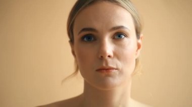 Sarı saçlı, bej arka planda kameraya poz veren doğal bir genç kadın portresi. 