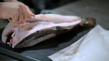 Kadın aşçı mutfakta bıçakla balığı kesiyor. 