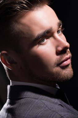 Siyah arka planda poz veren takım elbiseli yakışıklı bir adamın portresi.