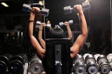 Siyah saçlı, kaslı, güzel bir kadın spor salonunda poz veriyor.