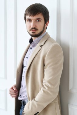 Beyaz duvar arkasında poz veren ceketli yakışıklı bir adam.