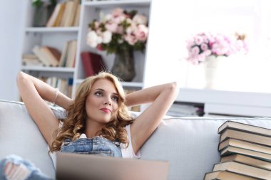 Eğitim. Kanepede oturan bir kadın, bir yığın kitapla çevrili.