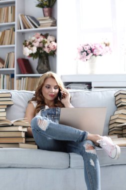 Eğitim. Kanepede oturan bir kadın, bir yığın kitapla çevrili.