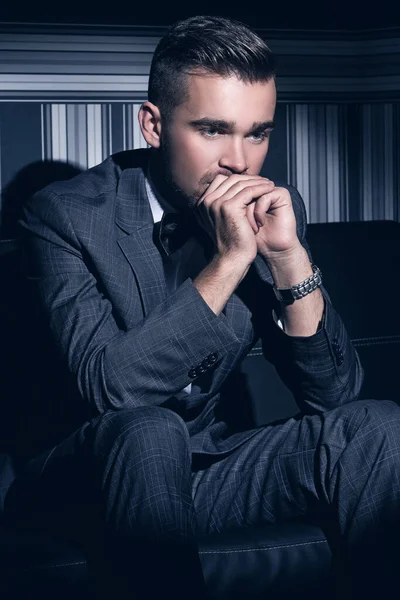 縞模様の背景にスポットライトに座っているスーツのハンサムな男の肖像画 — ストック写真