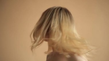 Sarı saçlı, bej arka planda kameraya poz veren doğal bir genç kadın portresi. 