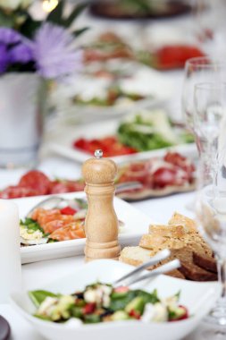 Bir kutlamada, içinde çiçekler ve bir sürü farklı yiyecek olan büyük bir yemek masası.