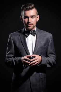 Siyah arka planda poz veren takım elbiseli yakışıklı bir adamın portresi.