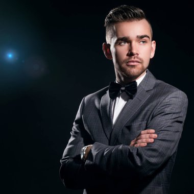 Arkasında mavi parçacıklar olan siyah bir arka plan üzerinde poz veren takım elbiseli yakışıklı bir adamın portresi.