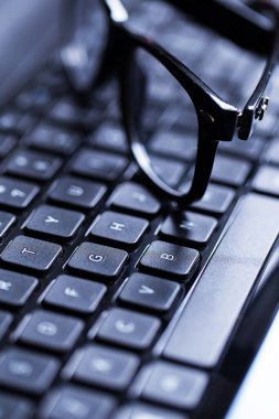 Üzerinde gözlük olan parlak bir dizüstü bilgisayarın yakın plan fotoğrafı.