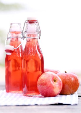 Yanında kırmızı içecek ve peçetenin yanında elma olan iki şişe.