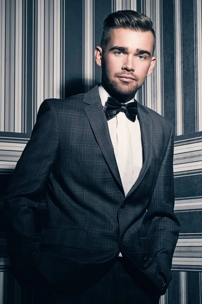 Çizgili arka planda poz veren takım elbiseli yakışıklı bir adamın portresi.