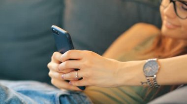 Evde akıllı telefon kullanan genç bir kadın.