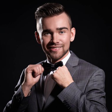 Siyah arka planda poz veren takım elbiseli yakışıklı bir adamın portresi.