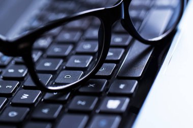 Üzerinde gözlük olan parlak bir dizüstü bilgisayarın yakın plan fotoğrafı.