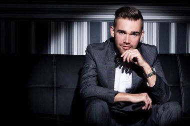 şeritli bir arka plan üzerinde koyu takım elbise ve kravat takan yakışıklı adam sakallı bir poz